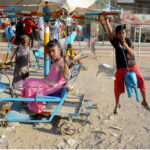 Children enjoy riding swing on a vendor’s setup on the third day of Eid al-Fitr in Chanesar Goth