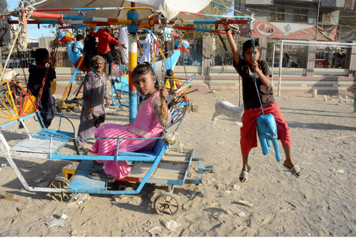 Children enjoy riding swing on a vendor’s setup on the third day of Eid al-Fitr in Chanesar Goth