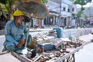 Battered by the blazing sun, a street vendor seeks refuge under a worn-out umbrella while selling scrap to make ends meet at Akthar Colony.