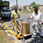 Labourers busy marking yellow line with a spray machine on main road