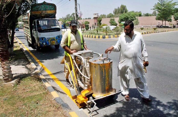 Labourers busy marking yellow line with a spray machine on main road