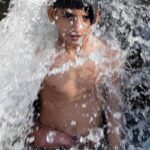 A young boy enjoys a splash in a running tube-well water tank to beat the scorching heat in the city