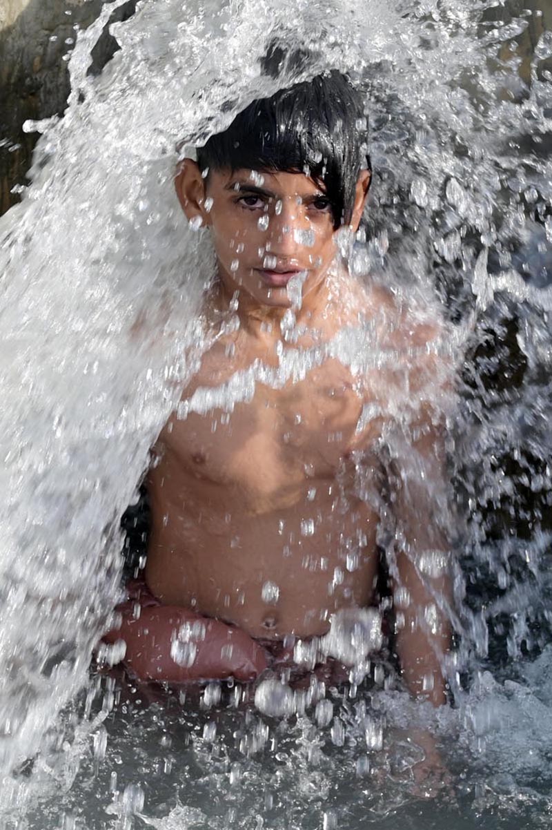 A young boy enjoys a splash in a running tube-well water tank to beat the scorching heat in the city