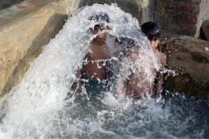 A young boy enjoys a splash in a running tube-well water tank to beat the scorching heat in the city
