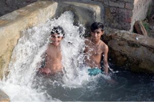 A young boy enjoys a splash in a running tube-well water tank to beat the scorching heat in the city