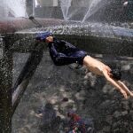 Youngster enjoy diving for bathing from leakage water supply line over the water canal during hot weather in the city