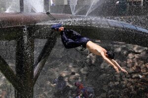 Youngster enjoy diving for bathing from leakage water supply line over the water canal during hot weather in the city