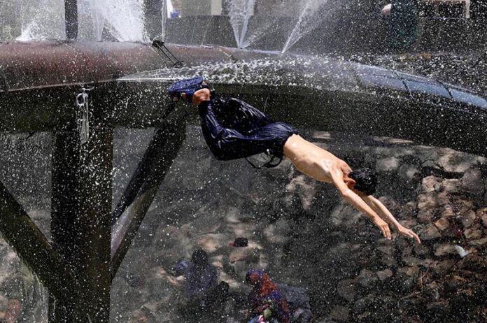 Youngster enjoy diving for bathing from leakage water supply line over the water canal during hot weather in the city