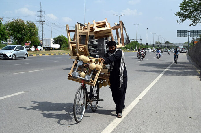 A vendor with a bicycle loaded with household items shuttles along the Expressway in the Federal Capital