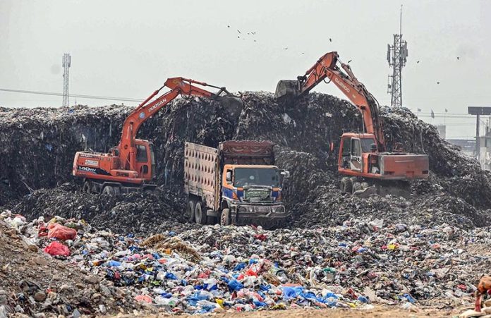 Heavy machinery being use for clear a large pile of garbage from garbage yard near fruit and vegetable market in federal capital