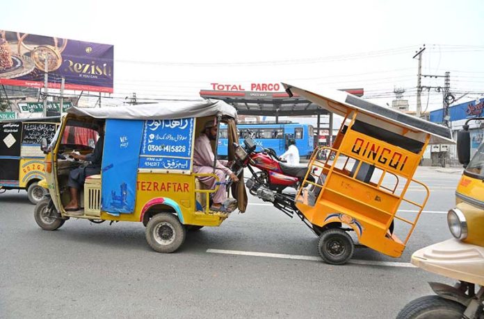 A person sitting on an auto rickshaw while holding an out of order tricycle at Khayyam Chowk