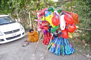 A roadside vendor rests while waiting for customers to sell colorful balloons of various shapes during scorching heat of the Federal Capital.