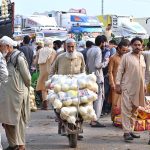 An elderly man pushes a handcart loaded with fresh ripe yellow melons, transporting them through the fruit and vegetable market in federal capital