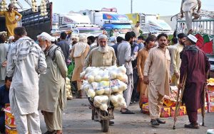 An elderly man pushes a handcart loaded with fresh ripe yellow melons, transporting them through the fruit and vegetable market in federal capital