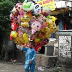 Young vendor selling colorful balloons to attract customers while shuttling on road in the Federal Capital