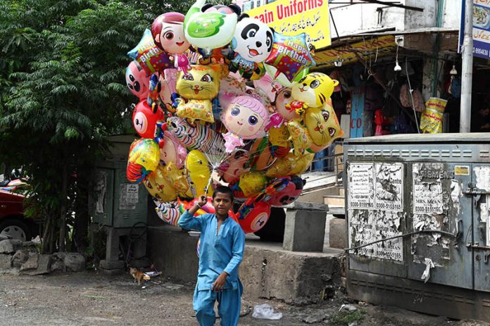 Young vendor selling colorful balloons to attract customers while shuttling on road in the Federal Capital
