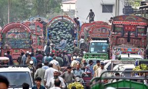 An elderly man pushes a handcart loaded with fresh ripe yellow melons, transporting them through the fruit and vegetable market in federal capital
