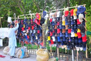 A vendor is busy arranging and displaying caps to attract customers at his roadside setup.