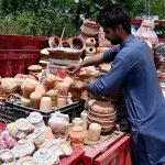 A vendor arranging and displaying clay made pots at his setup in the Federal Capital