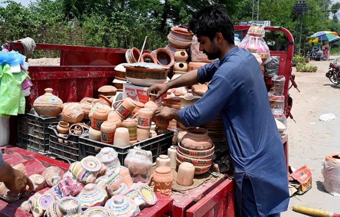 A vendor arranging and displaying clay made pots at his setup in the Federal Capital