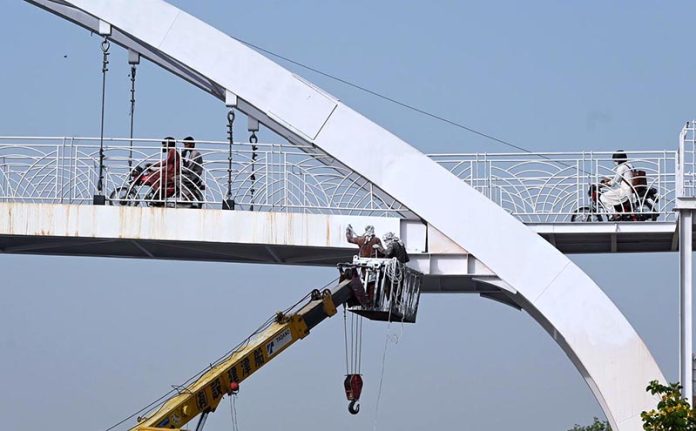 Laborers busy painting on pedestrian bridge at Srinagar highway in the Federal Capital