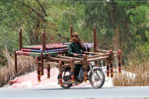 A motorcyclist on the way loaded with frames of a traditional bed (charpai) heading towards his destination.