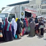 A long queue of needy people stands on the pavement waiting to receive free food from the Alamgir Welfare Trust's mobile food van
