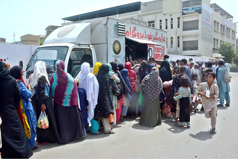 A long queue of needy people stands on the pavement waiting to receive free food from the Alamgir Welfare Trust's mobile food van