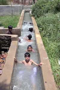 Youngster enjoying bathing in the running tube-well to get relief from scorching hot weather in the city.