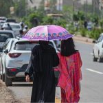 Women take shelter under umbrellas to shield themselves from the scorching sun on a hot summer day in the federal capital
