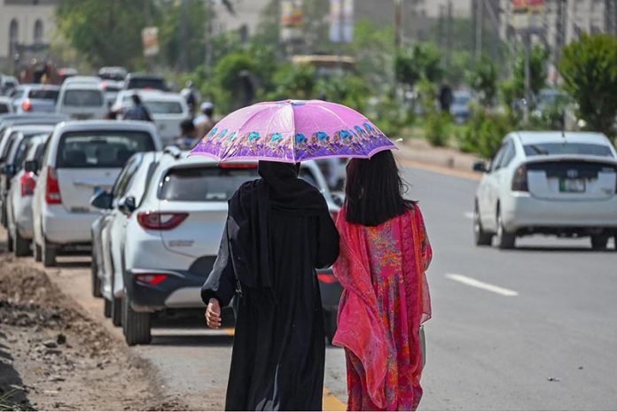 Women take shelter under umbrellas to shield themselves from the scorching sun on a hot summer day in the federal capital