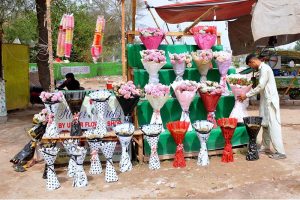 A vendor is busy arranging and displaying artificial flower bouquets to attract customers at his roadside setup.