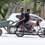 A man is sitting behind a motorcyclist, holding a handcart at College road