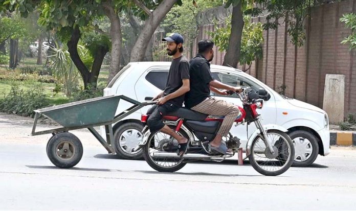 A man is sitting behind a motorcyclist, holding a handcart at College road