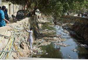 Amid the stench and sludge of a Korangi nullah, a man toils to fix a water pipeline.