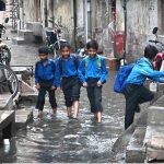 Students passing through rain water accumulated in the street at Imambara area after heavy rain in the city
