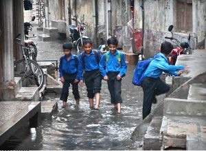 Students passing through rain water accumulated in the street at Imambara area after heavy rain in the city