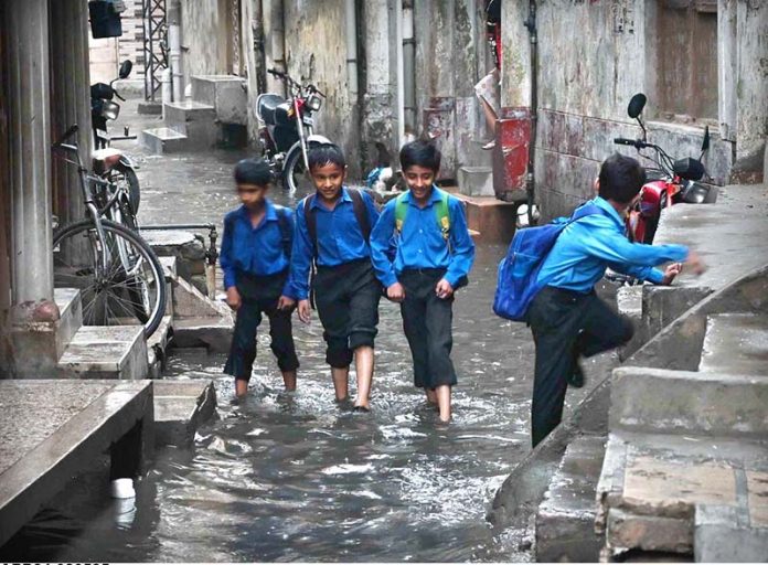 Students passing through rain water accumulated in the street at Imambara area after heavy rain in the city