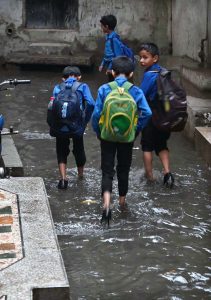 Students passing through rain water accumulated in the street at Imambara area after heavy rain in the city