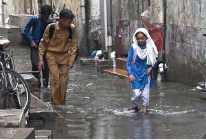 Students passing through rain water accumulated in the street at Imambara area after heavy rain in the city