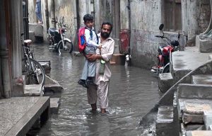 Students passing through rain water accumulated in the street at Imambara area after heavy rain in the city