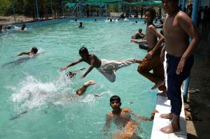 Youths dive into a swimming pool to beat the intense heat in Village Chooharpur near Larkana