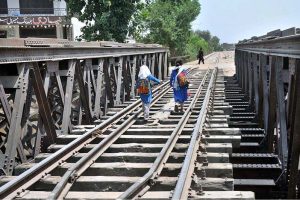 Schoolgirls cross a railway bridge on foot while returning home, reflecting the unsafe and challenging journeys many children endure daily in pursuit of education