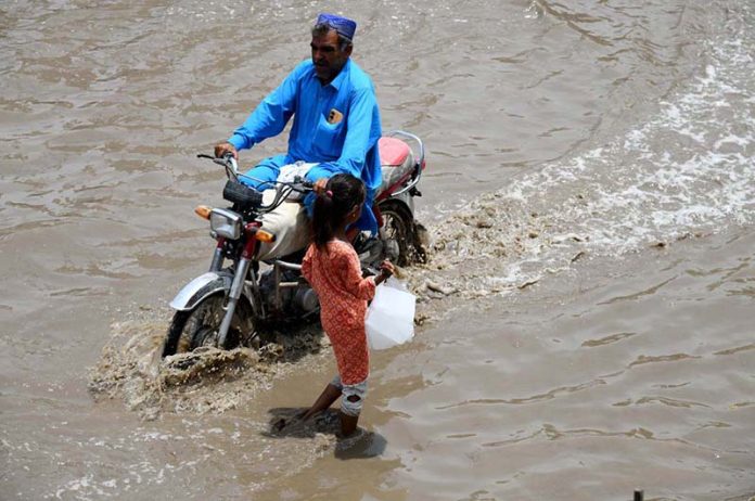 People make their way through stagnant rainwater accumulated on the road following heavy rainfall in the city