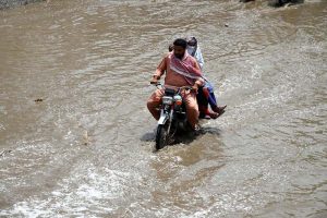 People make their way through stagnant rainwater accumulated on the road following heavy rainfall in the city