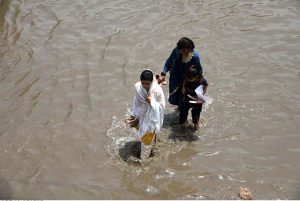 People make their way through stagnant rainwater accumulated on the road following heavy rainfall in the city