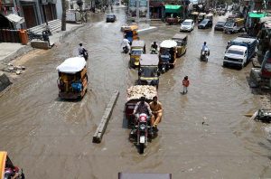 People make their way through stagnant rainwater accumulated on the road following heavy rainfall in the city