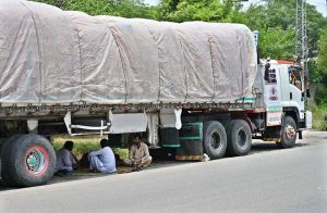 The staff of the 22-wheeler truck rest under the vehicle to protect themselves from the direct sunlight during the scorching heat.