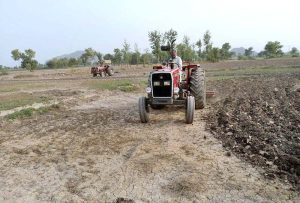 A farmer preparing land for next crop with help of tractor along Lahore Road