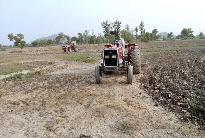 A farmer preparing land for next crop with help of tractor along Lahore Road